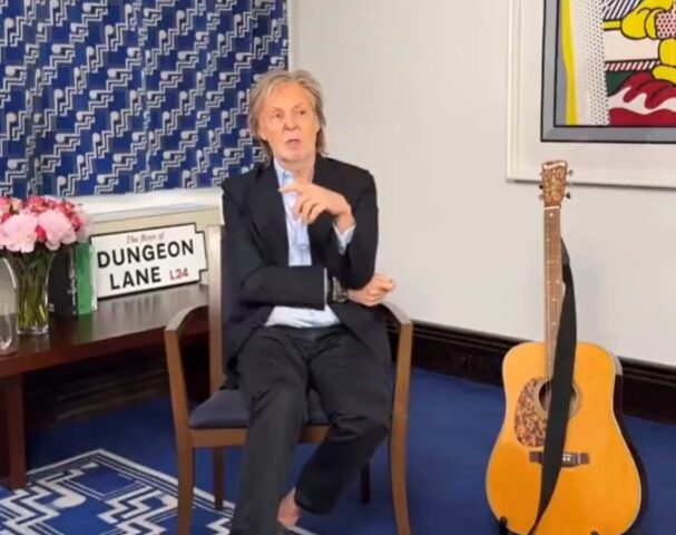 Paul McCartney durante evento promocional em frente a uma obra com os integrantes dos Beatles.